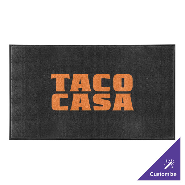 A black M+A Matting ColorStar Impressions custom logo mat with orange text that says "Taco Casa" on a table.