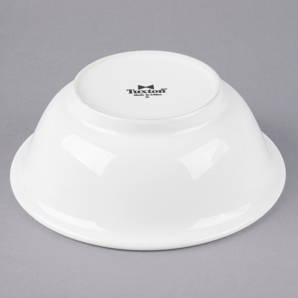 A white Tuxton footed salad bowl with a black rim on a gray background.