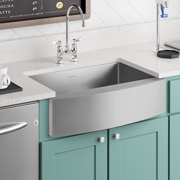 An American Standard stainless steel farmhouse sink in a kitchen with a white counter.