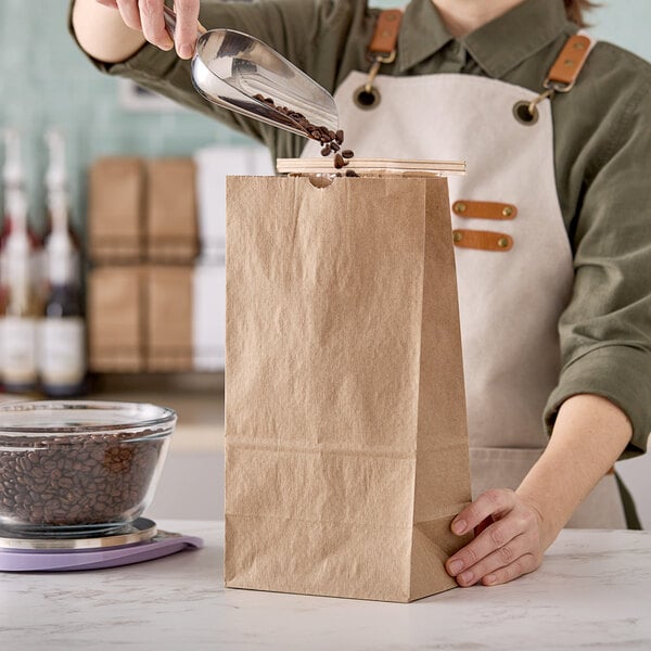A person pouring coffee beans into a brown paper bag.