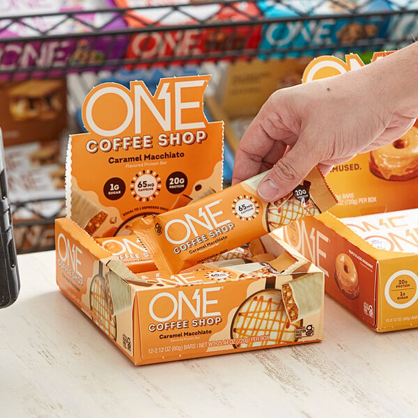 A hand holding a box of ONE Coffee Shop Caramel Macchiato Protein Bars.