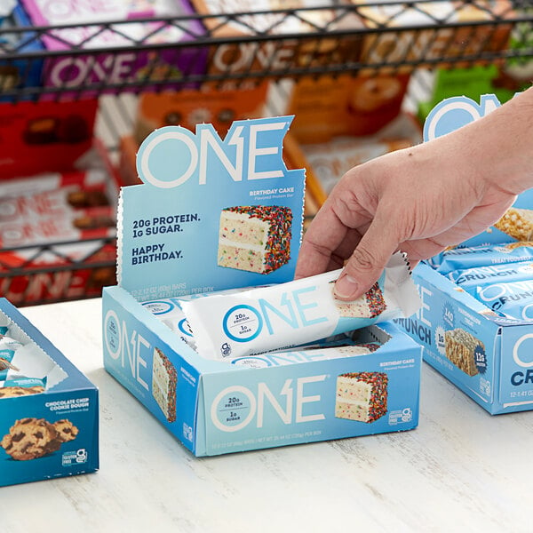 A hand holding a box of ONE Birthday Cake protein bars.