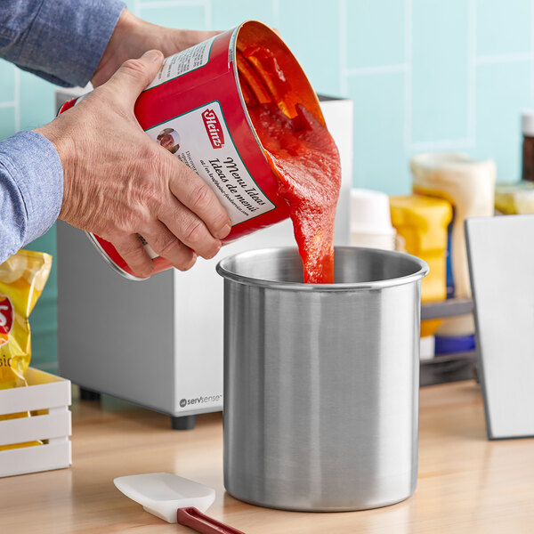 A person using a ServSense stainless steel condiment pump to pour red sauce into a container.