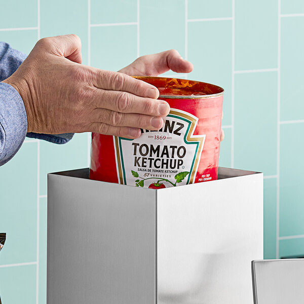 A person using a ServSense stainless steel condiment pump to dispense ketchup from a can.