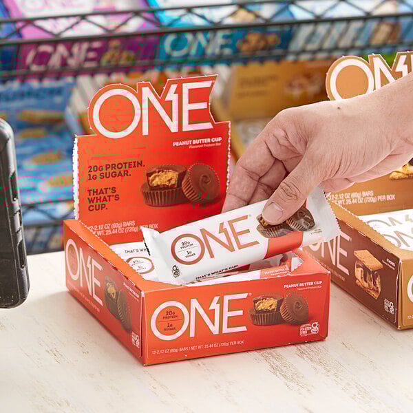 A hand taking a ONE Peanut Butter Cup Protein Bar package from a box.