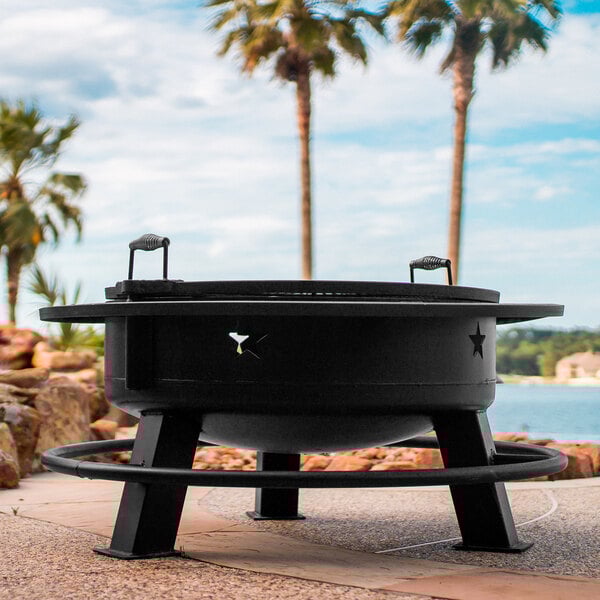 An Old Country BBQ Pits steel round fire pit with handles on a stone surface.