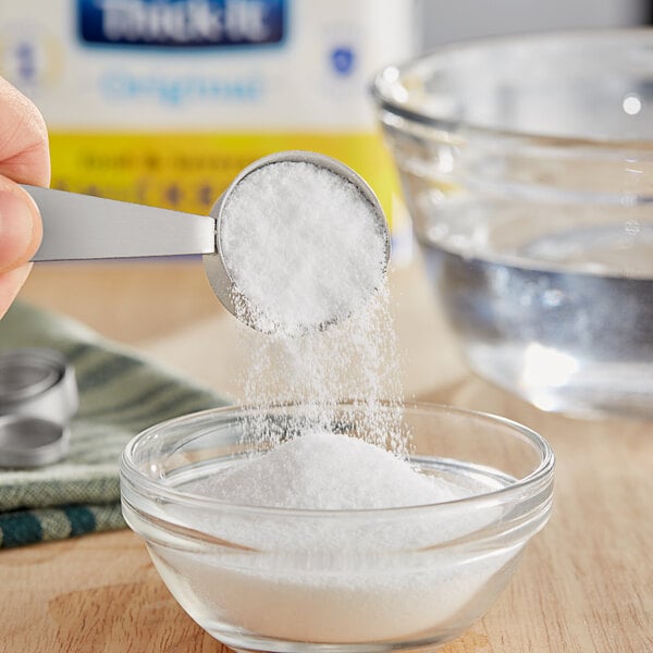 A measuring spoon with white powder being poured into a bowl.