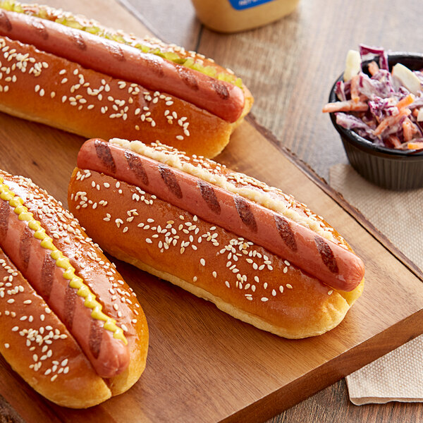 Three Sabrett beef hot dogs with mustard on a cutting board with coleslaw.