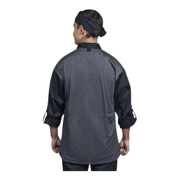 A chef wearing a black Uncommon Chef Roma long sleeve chef coat with a silver and grey mesh back.