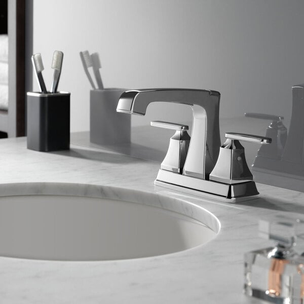 A Delta chrome deck-mount lavatory faucet with lever handles and a metal pop-up drain installed on a sink.