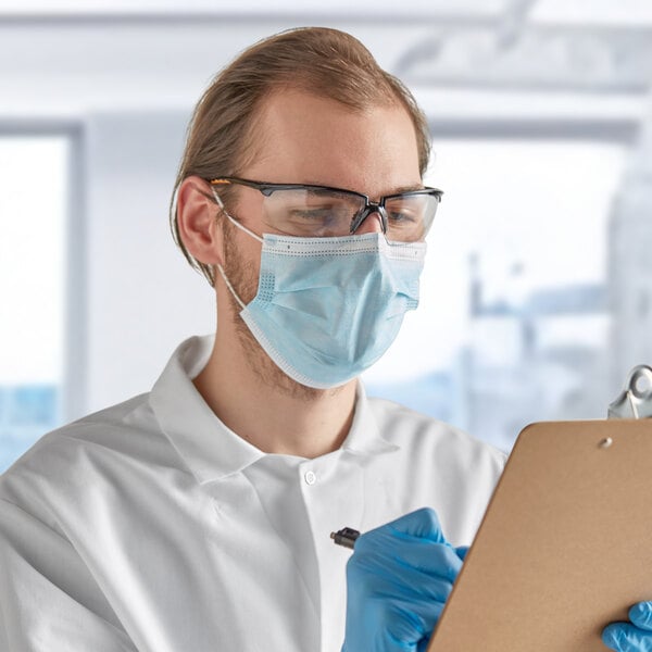 A man wearing a Lavex blue protective face mask and gloves writing on a clipboard.