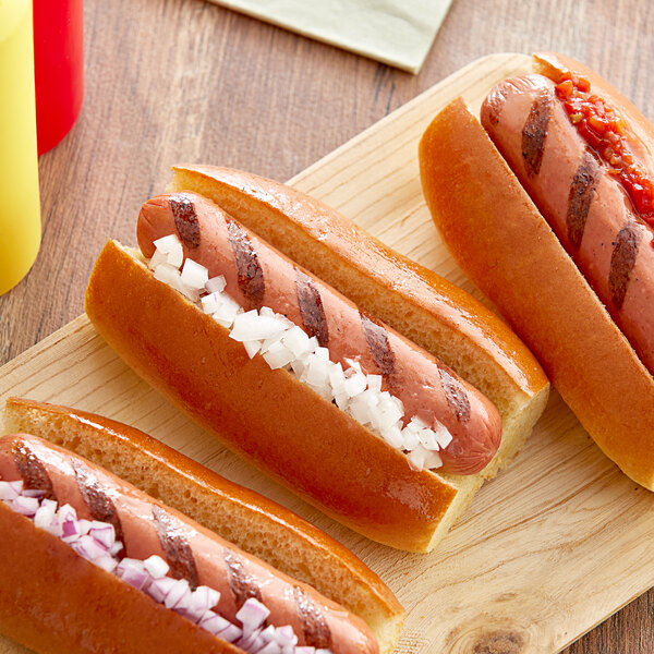 Three Sabrett beef hot dogs with ketchup, mustard, and onions on a wooden board.