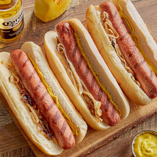 Three Vienna Beef Ditka hot dogs on buns with mustard and onions on a table in a stadium concession stand.
