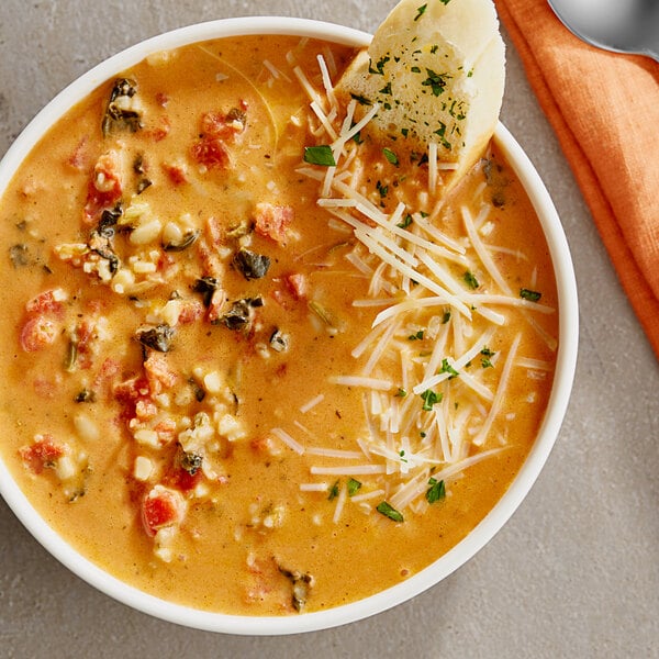 A bowl of tomato bisque with spinach and orzo topped with cheese and bread.