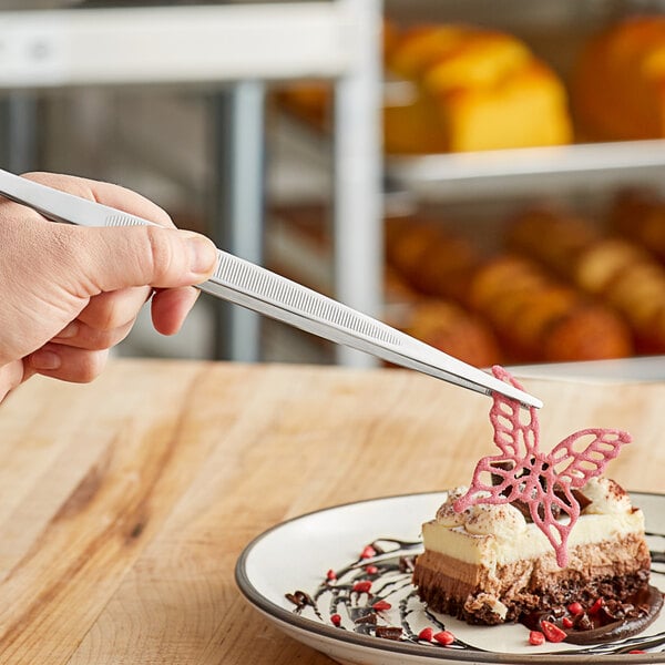 Mercer Culinary plating tongs used to serve a piece of cake on a plate.