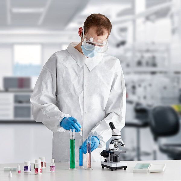 A man wearing a Lavex white microporous long sleeve lab coat and goggles holding a test tube.