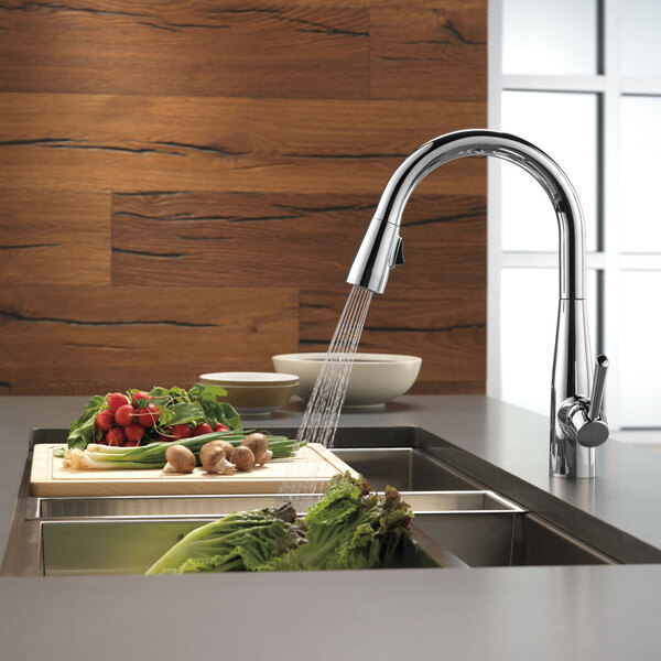 A Delta Essa kitchen faucet running water over vegetables on a cutting board.