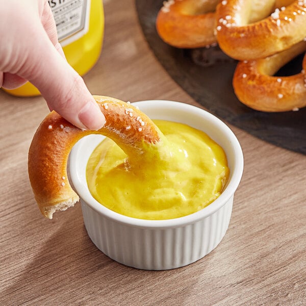 A person dipping a pretzel into a bowl of Heinz yellow mustard.