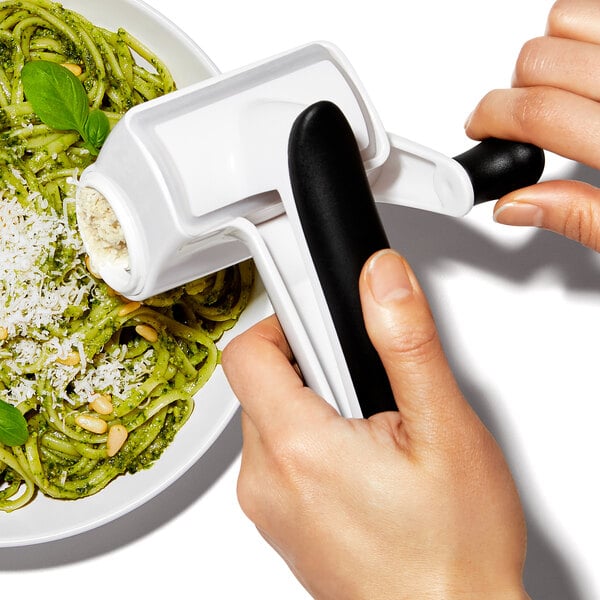 A person using the OXO Good Grips Rotary Grater to grate pasta over a dish.