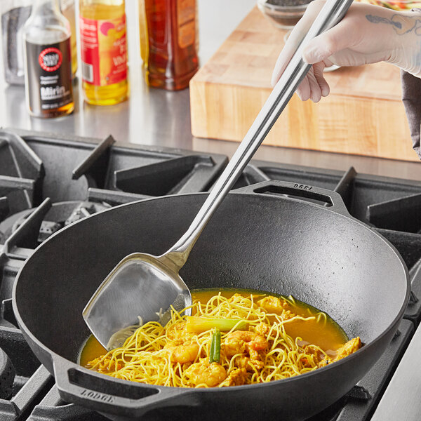 A person stirring noodles in a wok with a Town medium stainless steel wok spatula.