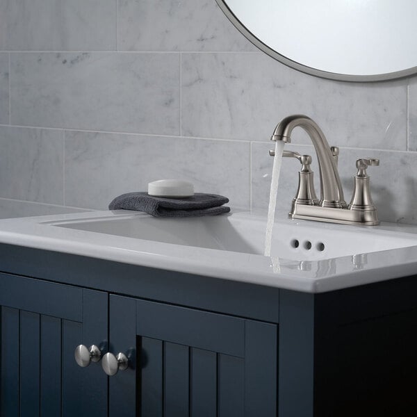 A bathroom sink with a Delta Woodhurst deck-mount faucet with stainless finish and lever handles running into the sink.