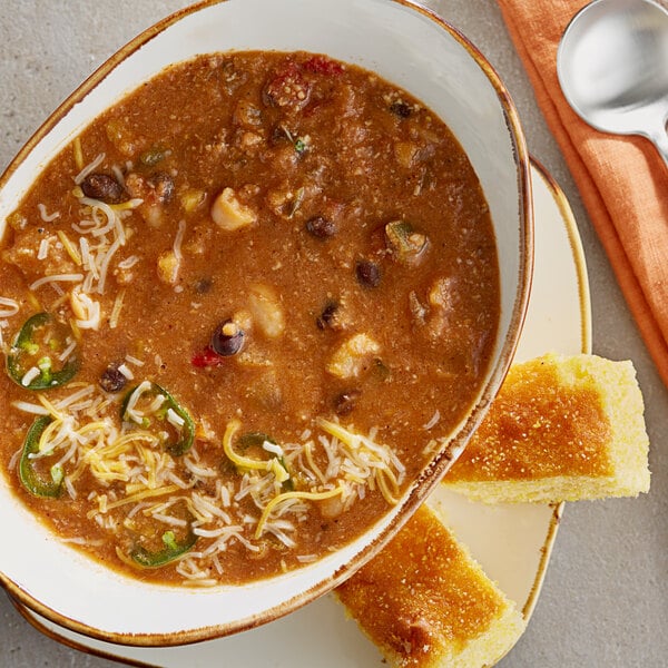 A bowl of Vienna Beef Sweet Heat Turkey Chili with a spoon and cornbread on a plate.