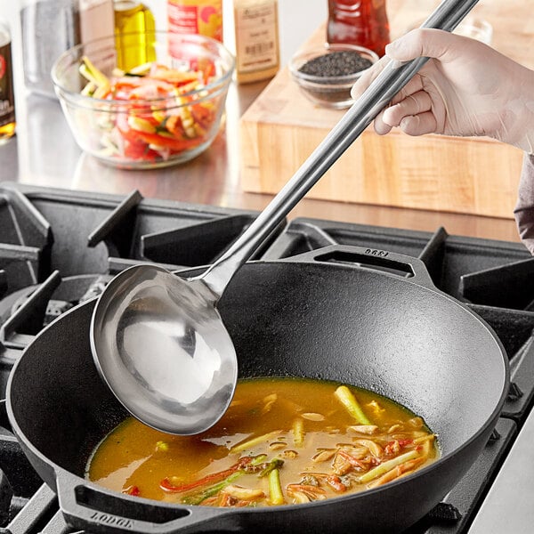 A hand holding a Town Stainless Steel Wok Ladle over a pan of soup.