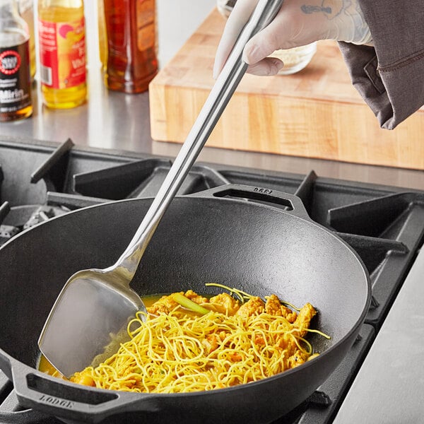 A person using a Town large stainless steel wok spatula to stir noodles in a pan.