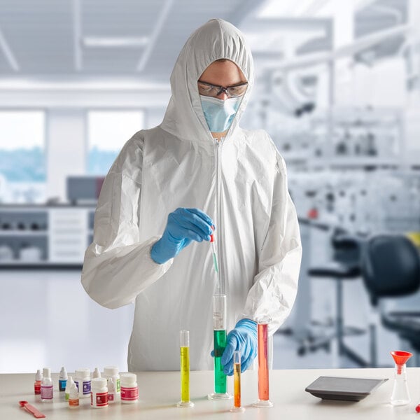 A man in a white Lavex protective suit and gloves pouring liquid into a test tube.