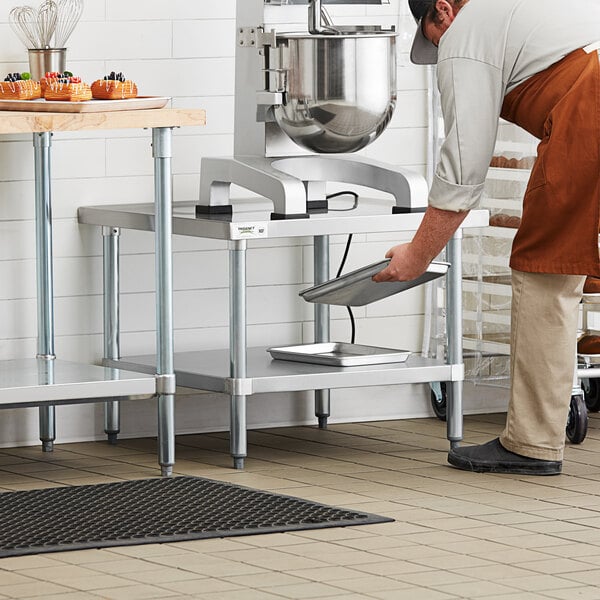 A man in an apron and hat working on a Regency stainless steel mixer table.