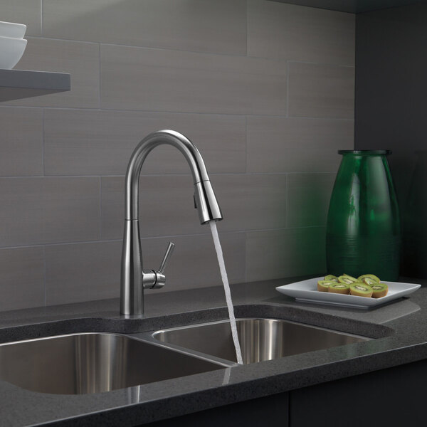 A kitchen sink with a Delta Essa kitchen faucet running water.