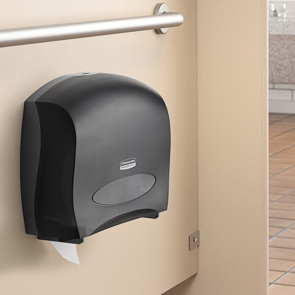 A black Kimberly-Clark Professional jumbo roll toilet paper dispenser on a wall.