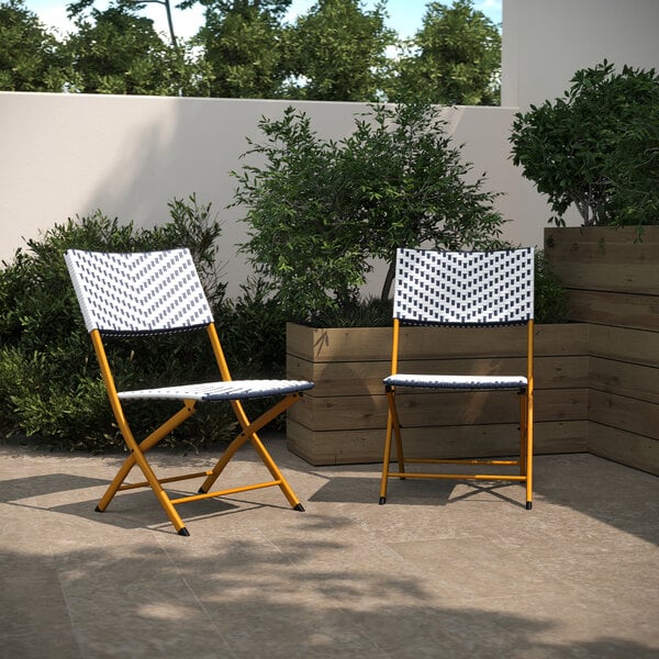 Two Flash Furniture folding chairs with navy and white synthetic rattan on a patio.
