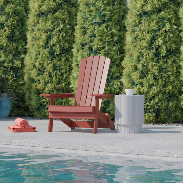 A red Flash Furniture Charlestown faux wood Adirondack chair sitting next to a pool.