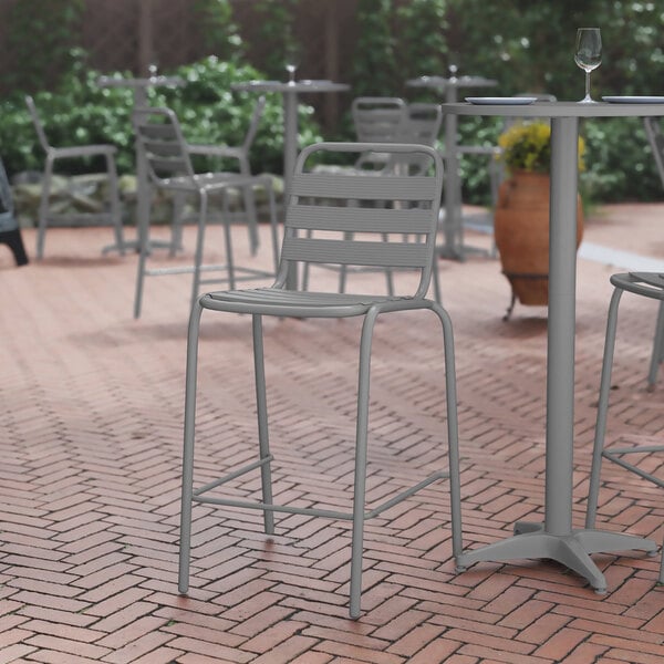 A Flash Furniture silver aluminum slat bar stool on a brick patio.