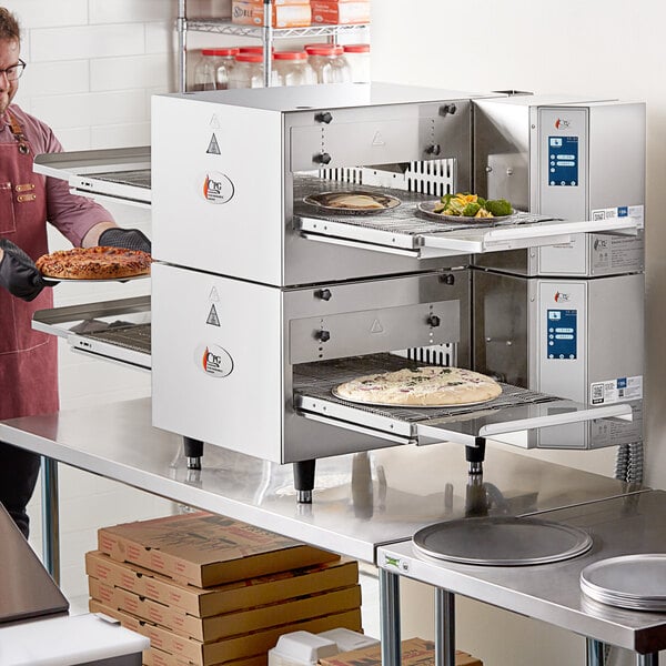 A man in an apron using a Cooking Performance Group countertop conveyor oven to cook a pizza.