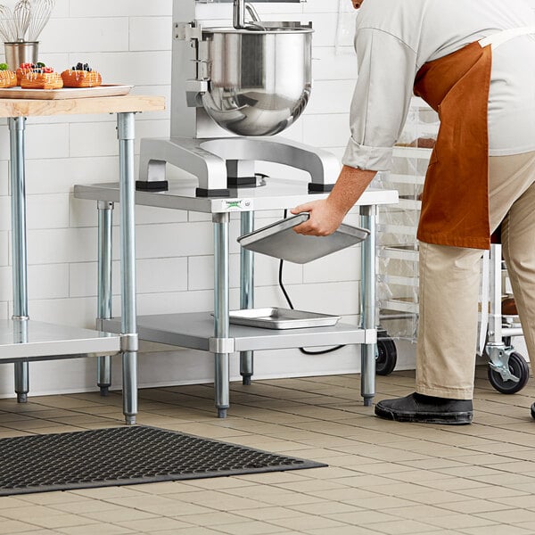 A man in an apron working at a Regency stainless steel mixer table with a metal container.