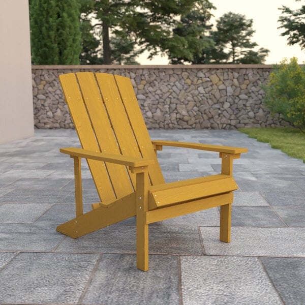 A yellow Flash Furniture Charlestown wooden Adirondack chair on a stone patio.