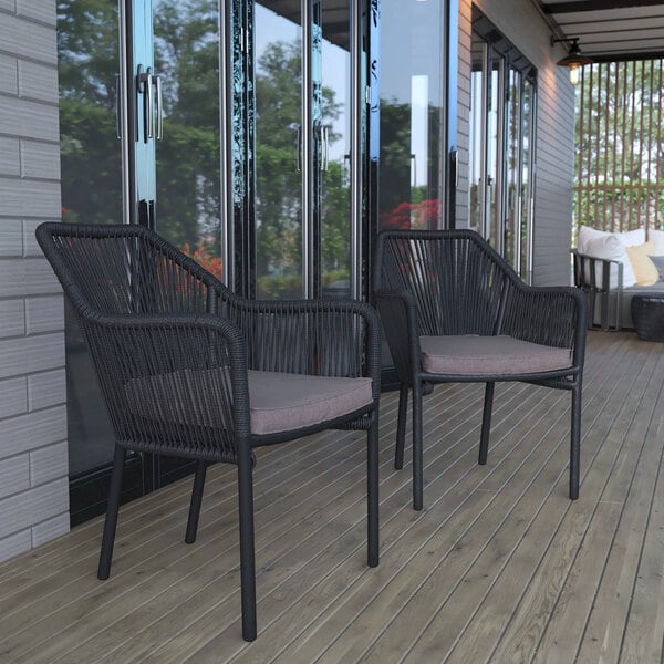 Two Flash Furniture Kallie black synthetic wicker arm chairs with gray cushions on a deck.