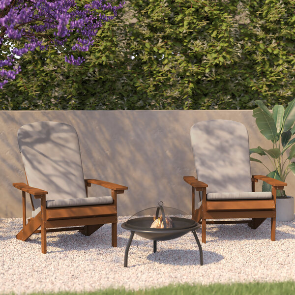 Two Flash Furniture teak Adirondack chairs with cream cushions in front of a fire pit.