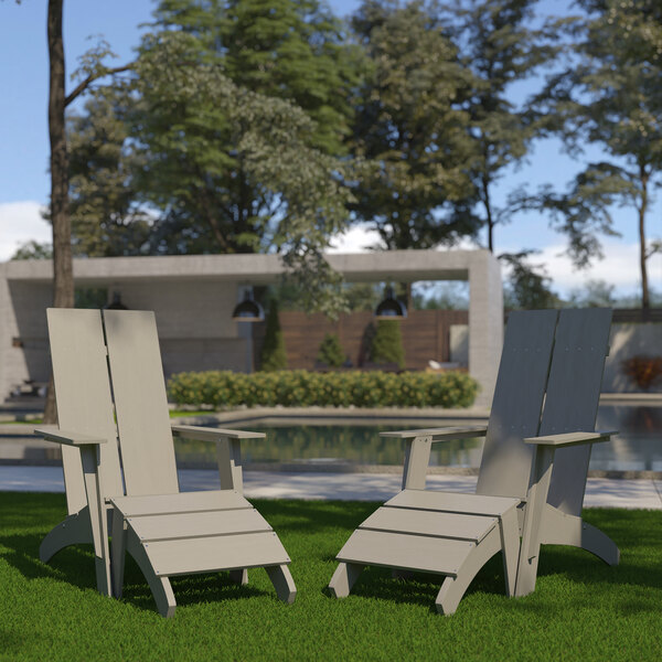 Two gray faux wood Adirondack chairs with ottomans on grass