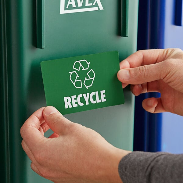 A person putting a Lavex Recycle Waste Stream label on a green recycle bin.