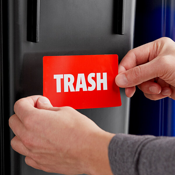 A person putting a red sign into a black trash can.