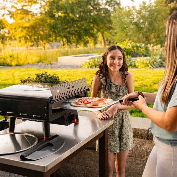 A woman and girl using a Blackstone Leggero Liquid Propane Pizza Oven on a table outdoors.