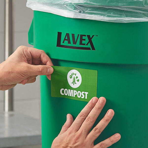 A hand putting a Lavex compost label on a green bin.