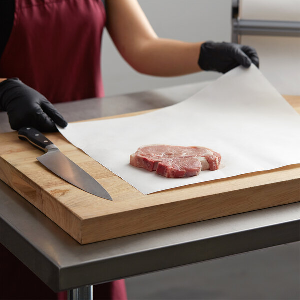 A person in an apron and gloves using Choice Freezer Paper to wrap meat on a cutting board.