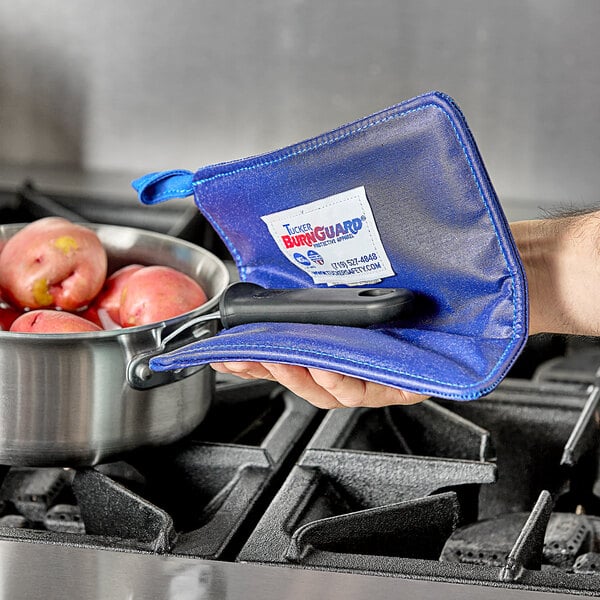 A person using a Tucker Safety blue poly-cotton hot pad to hold a pot of apples.