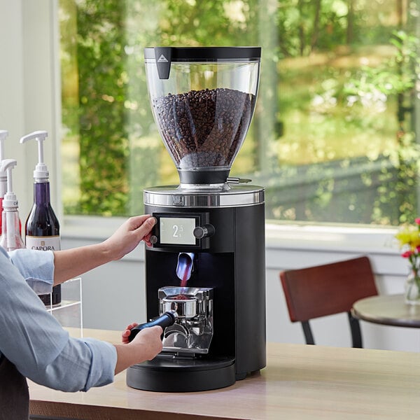 A person using a Mahlkonig black espresso grinder on a wooden surface.