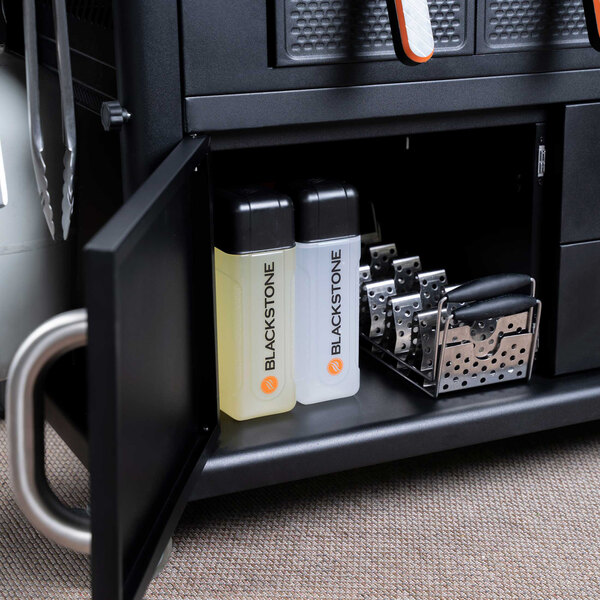 The interior of a Blackstone outdoor griddle with cabinets and a shelf with bottles and lighters.
