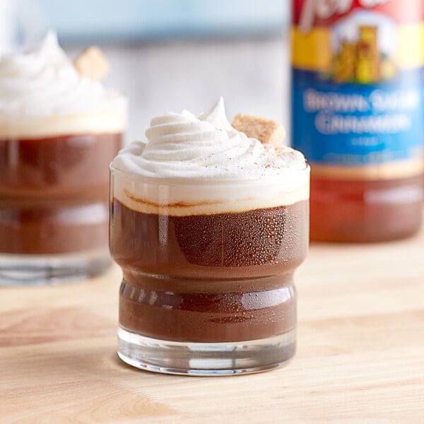 A glass of chocolate pudding with whipped cream and brown sugar next to a bottle of Torani Brown Sugar Cinnamon Flavoring Syrup.